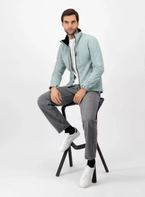 Hombre sentado usando chamarra de color azul claro, pantalones gris y tenis blancos.