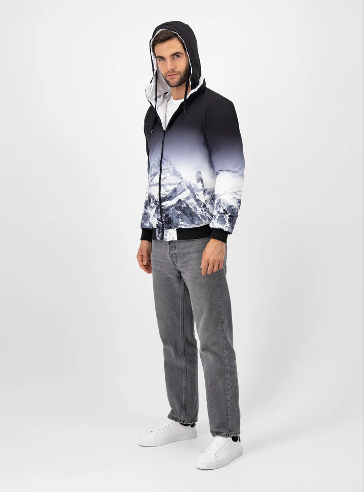 Hombre usando chamarra de color negro con blanco, pantalones grises y tenis blancos.